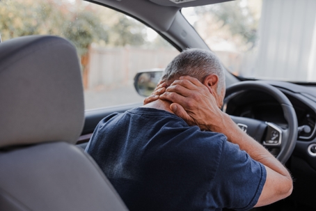 A man sitting in a car, holding his neck in pain. | The Law Offices of Anthony Urban, P.C.